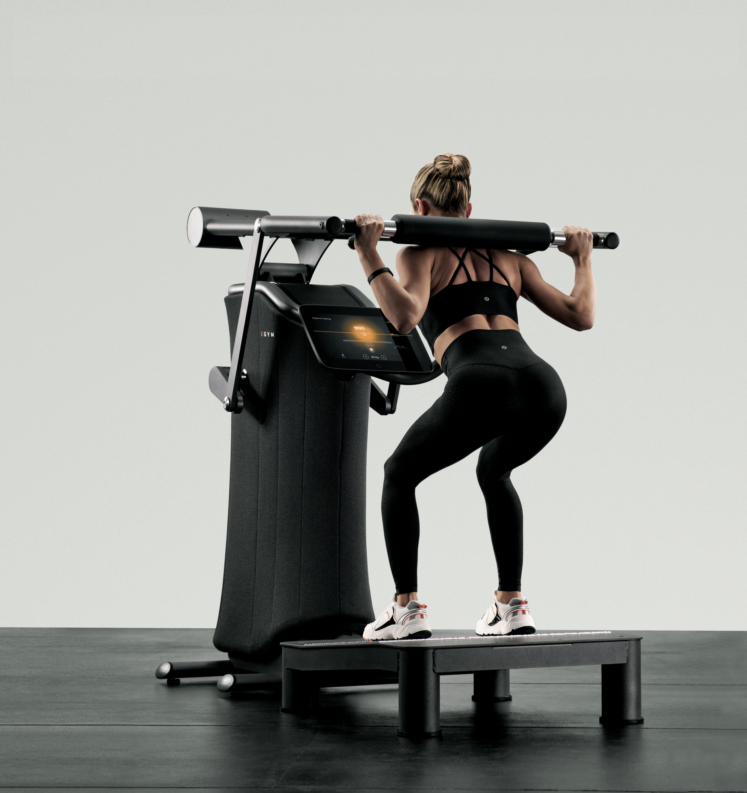 Sportlerin führt eine Kniebeuge an einem EGYM Kraftgerät mit digitalem Display aus.