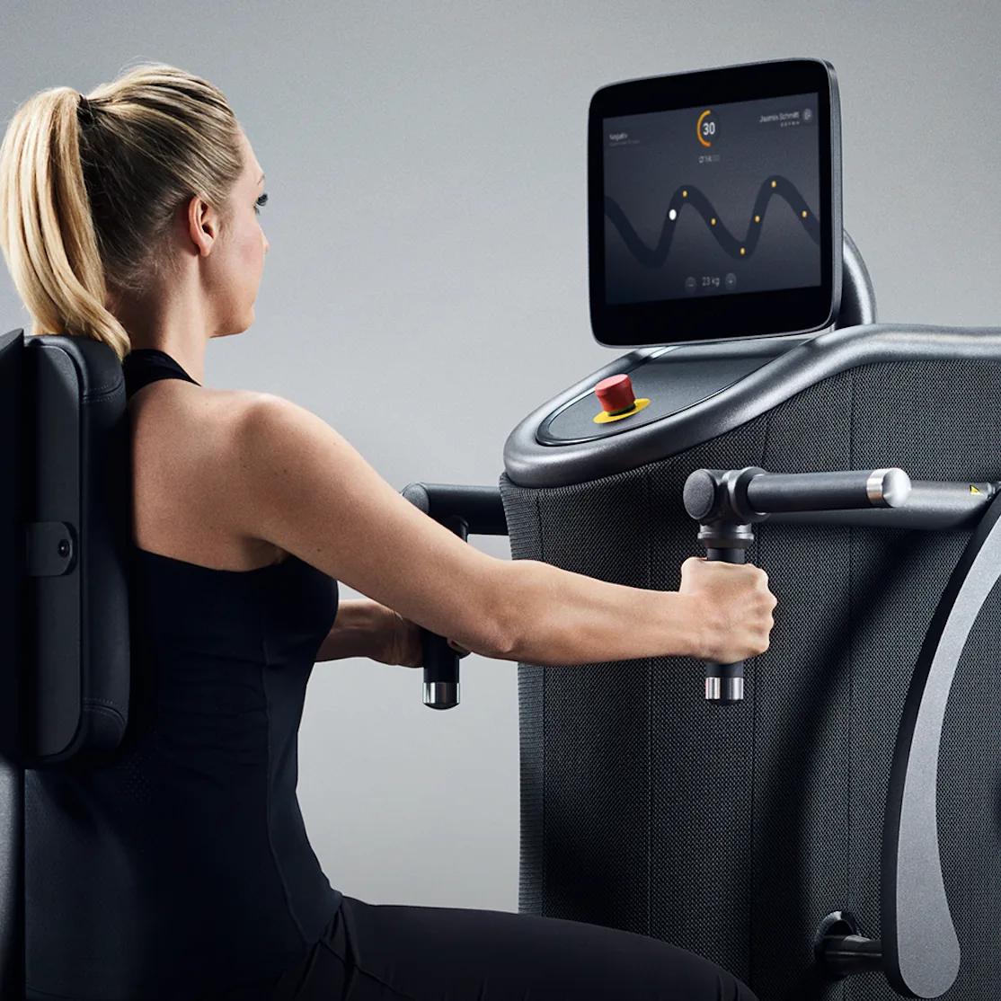 Frau beim Oberkörpertraining an einer computergesteuerten Armpresse, der Bildschirm zeigt den Bewegungsverlauf